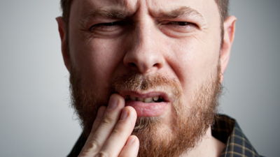 Man with beard holding cheek because of severe tooth pain.