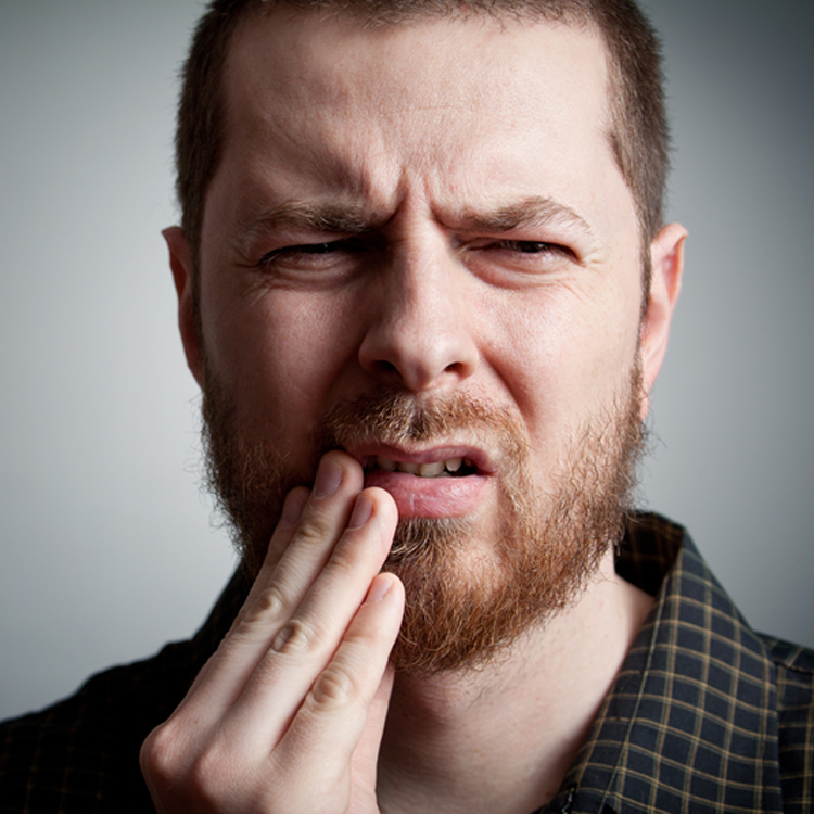 Man with beard holding cheek because of severe tooth pain.