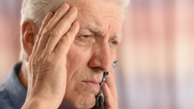 Elderly man with his hand on his head, holding his tooth in pain